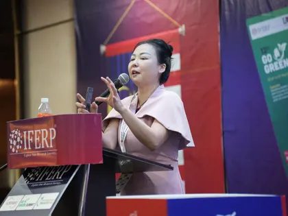 A speaker presenting with a slide remote at the IFERP podium